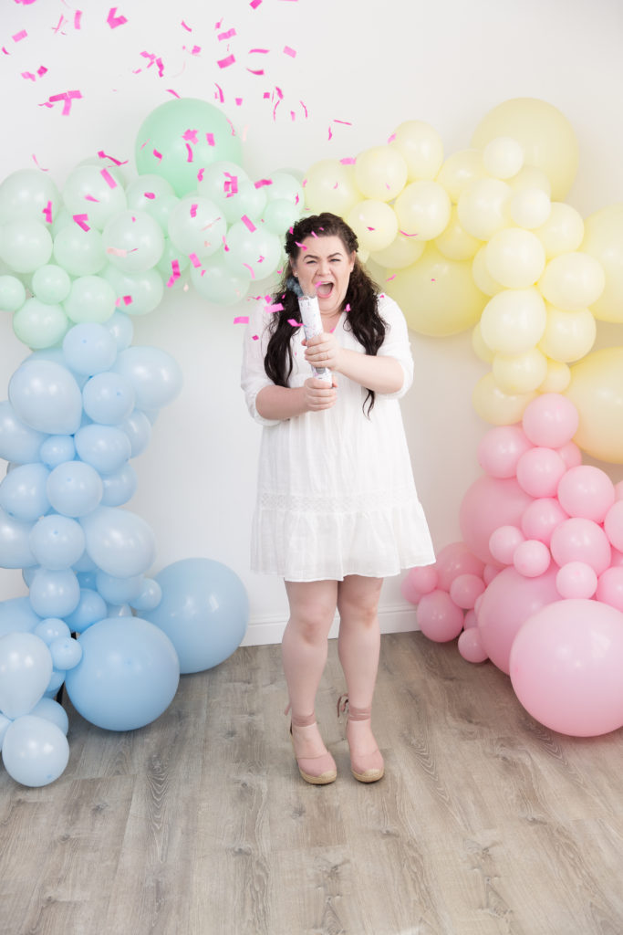 Baby girl gender reveal with pastel rainbow balloon garland pink confetti