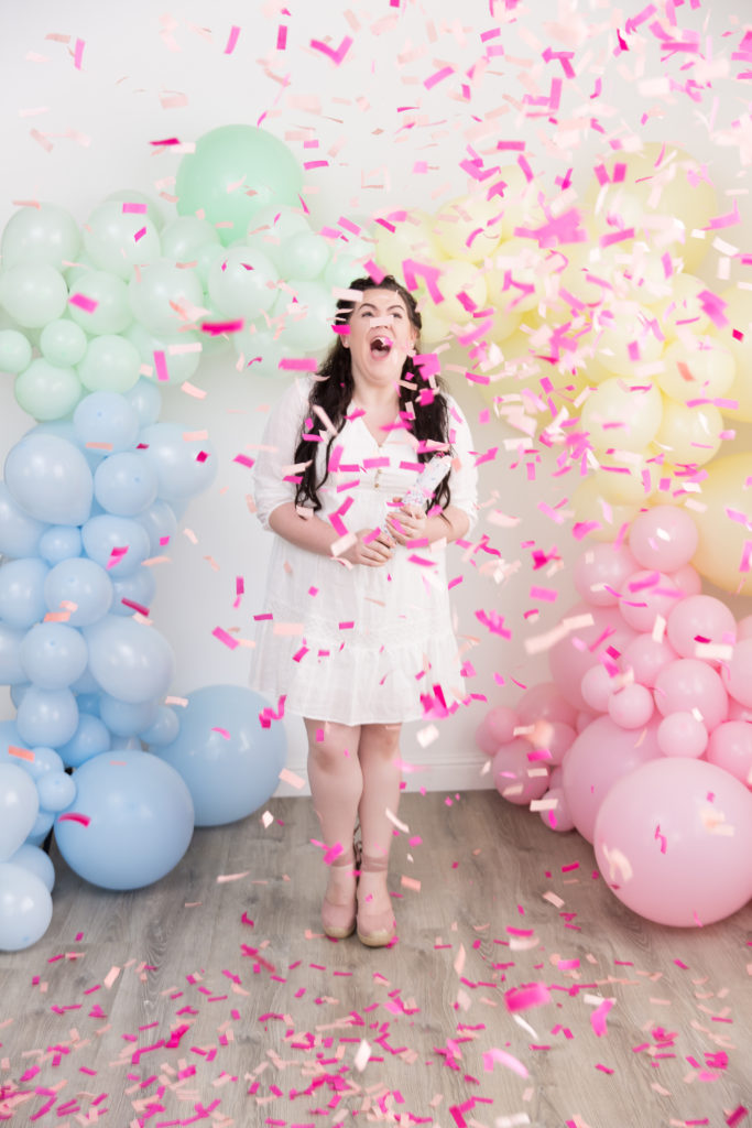 Baby girl gender reveal with pastel rainbow balloon garland pink confetti