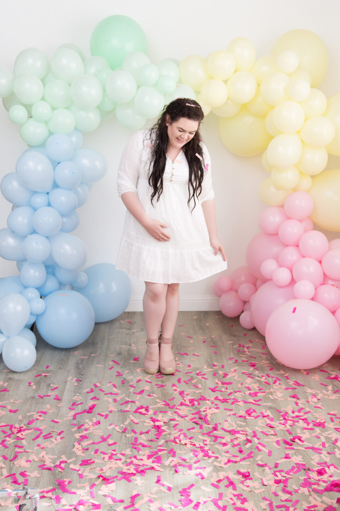 Baby girl gender reveal with pastel rainbow balloon garland