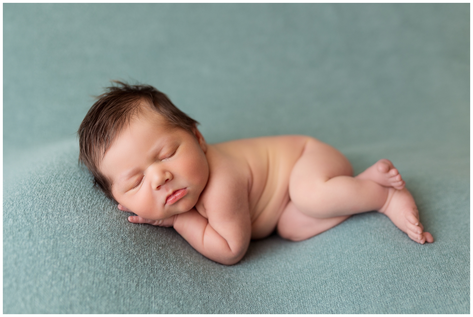 posed newborn boy on a teal blanket with lots of hair
